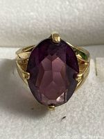 Front view of ring showing oval purple amethyst in gold prong setting on white foam.