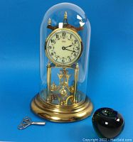 Front view of clock under glass dome with winding key and green glass apple (size reference)