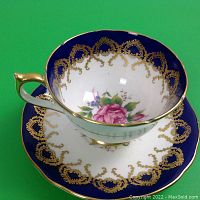 Top view of Aynsley cup sitting on matching saucer, showing the detailed gilt pattern inside the cup and floral design at bottom.