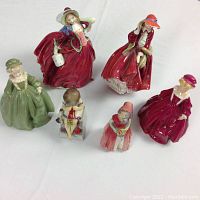 Six collectible porcelain figurines arranged together including women and children in period dresses and hats.