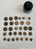 Layout of thirty-one assorted coins on white cloth with a green apple for size reference. Coins range in size and design.