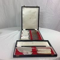 Open box with two stacked trays showing fish knives and forks on red velvet interior.