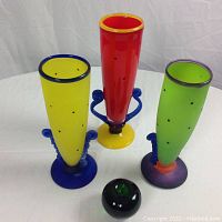 Photo showing three vibrant colored art glass vases: yellow, red, and green with a small black and green orb in front for size reference.
