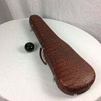 Closed hard shell case with brown faux crocodile exterior and green glass sphere for scale