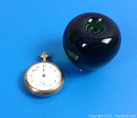 Watch next to a green glass apple for size reference on blue background.