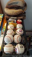 10 signed baseballs arranged in a crate with visible player photos and signatures. 3 worn Mizuno baseball gloves stacked behind the baseballs. Sticker albums with baseball cards in the same crate.