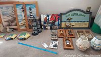 Full view of all beach themed items including framed lighthouse art, lighthouse figurines, ceramic fish, wooden mirrors, candle holders, and decorative plaques arranged on floor.