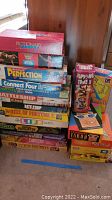 Stack of assorted board games including Pictionary, WWE Wrestling Game, Perfection, Connect Four, Battleship, Wheel of Fortune, Life, Careers, and Taboo.
