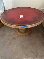 Side angle photo showing the red leather top with gold border and part of the carved wooden pedestal base.