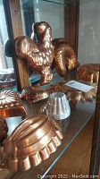 Multiple copper form pans displayed on glass shelves including poultry, fish shapes and round fluted pans.