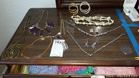 Overview of lot showing multiple pieces of costume jewelry arranged on a brown wooden surface including necklaces, bracelets, and earrings in various styles and colors