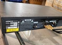 Rear view of the Hitachi DV P315U DVD player showing audio-video connections, model and serial number labels, and safety warnings.