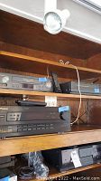 Kenwood CD player, Sharp VHS players on wooden shelves with remotes visible.