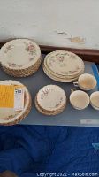 Full set of floral designed plates, cups, and bowls with gold rims arranged on a surface showing quantity and variety.