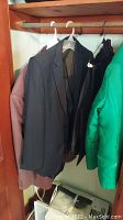 Photo of mens suits and jackets hanging on a wooden rod inside closet.