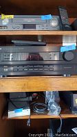 Photo showing two audio-video receivers with remote control on top shelf and other electronics below.