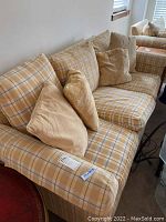 Photo of Rowe sofa with yellow, grey, and white plaid throw pillows and armrest covers against a white wall.