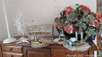 Wooden cabinet top with vintage sewing box, spools of thread, lace doilies, and artificial floral arrangement