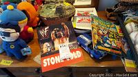 Photo showing South Park plush dolls, Stone Cold WWE poster, diecast blue car model, and Star Wars figures basket grouped on table.
