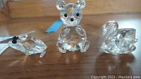 Clear Swarovski crystal bear, frog prince, and swan figurines on wooden surface with natural lighting