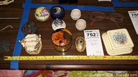 Photo of assorted trinket boxes and eyeglasses on a wooden surface with a measuring tape for scale.