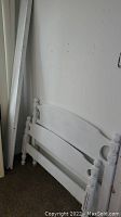 Photo of the wooden twin bed frame headboard painted white, showing the curved top and turned post finials against a wall.