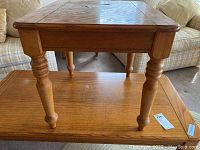 Side view of wooden side table showing turned legs, wood grain, and general condition with some surface scuffs and scratches.