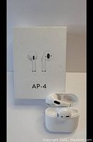 Photo showing white AP-4 wireless earbuds placed in the charging case next to the white retail box with AP-4 branding and earbud image on front.