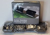 Image shows one boxed Codian Solar Garden Railing Light and multiple individually plastic-wrapped units stacked below it.