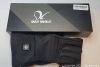 Photo of a pair of black Day Wolf rechargeable heated gloves with visible heating control button, displayed alongside the original Day Wolf branded box.