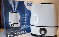 White ultrasonic humidifier alongside its original box showing features such as essential oil tray, 6L water tank, auto shut-off, and filterless design.
