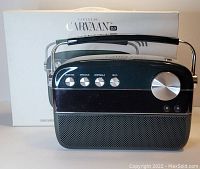 Front view of Saregama Carvaan 2.0 black and green Wi-Fi audio player with silver volume knob and buttons, with original box in background.