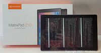Photo showing Vankyo MatrixPad Z10 tablet placed next to its retail box packaging. Box white with product image and orange Vankyo logo. Tablet screen is black and reflective.