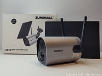 Photo showing Zumimall GX1K security camera alongside its solar panel and retail box, highlighting camera and solar power capabilities.
