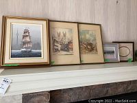Wide view of five framed pieces displayed on a shelf
