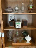 Two shelves of compote bowls, bowls and wood tray displayed inside a wooden cabinet, including glass and milk glass items.