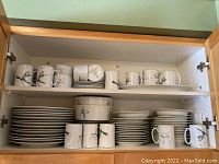 Full view of all dishes inside a cabinet showing stacks of dinner plates, lunch plates, bowls, mugs, and teacups with saucers all decorated with trillium flowers.