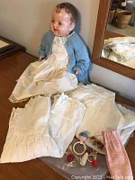Antique doll seated, showing white cotton petticoats and small vintage doll toys on table