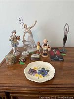Overview of all items on wooden dresser showing figurines, trinket boxes, plate, and metal sculpture