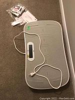Overview of gray rectangular vibration plate with coiled power cord and assorted manuals, remote, DVD