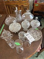 Group photo of glass and crystal items on table including domed compote bowls, pitcher, glasses, and bowl