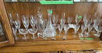 Wide view of entire glassware collection on wooden shelf, showing two decanters and multiple glasses