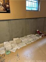 Long view of assorted white table linens and napkins laid on basement floor against concrete wall.