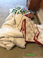 Overall view of bedding and textiles including comforter, quilted linen piece, pillows, and blankets.