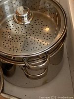Large stainless steel pot with perforated lid for steaming, showing handles and shiny finish