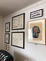 Wall display of seven framed prints including three vintage style maps (one likely of the Americas), an Egyptian pharaoh mask print on papyrus, and a black and white cityscape skyline.