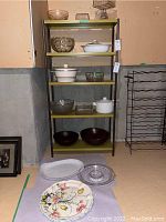 Full view of shelving unit displaying assorted serving ware including glass bowls, lidded pots, and decorative plates on surrounding floor space.
