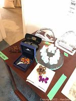 Table display of all lots including Swarovski brooch in box, two brooches, eyeglasses, comb, and glass art pieces on mirror base