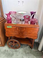 Wood tea cart with removable glass insert top tray, holding various glassware. Visible ornate large wooden wheels and polished wood surface.