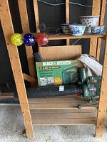 Photo of Black and Decker garden vacuum with original box and attachments on wooden shelf with solar lights and pots in background.